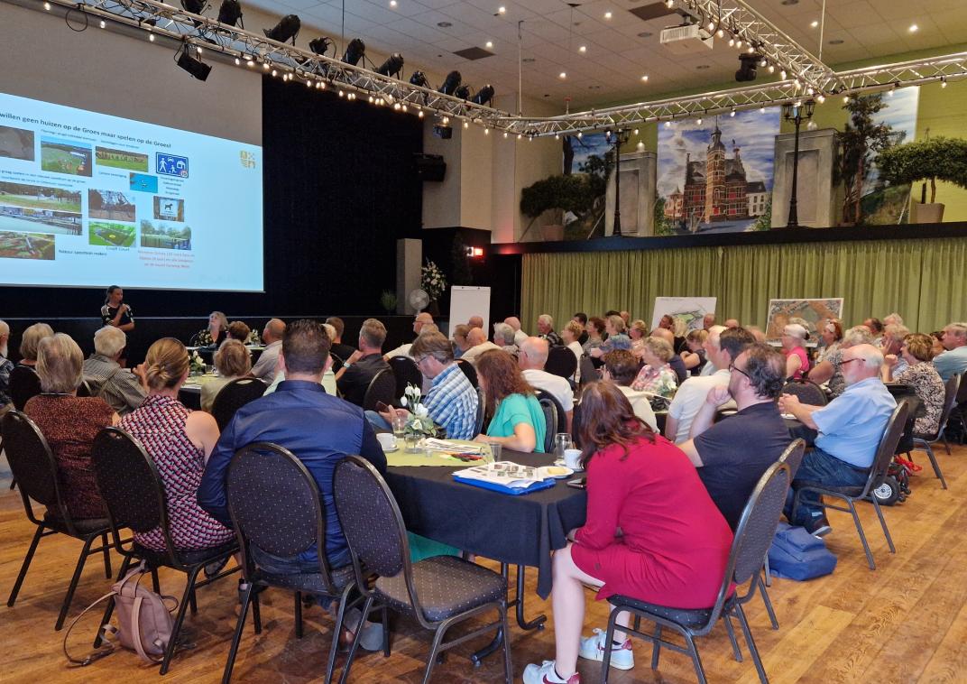 Bezoekers bekijken vanaf lange tafels de presentatie