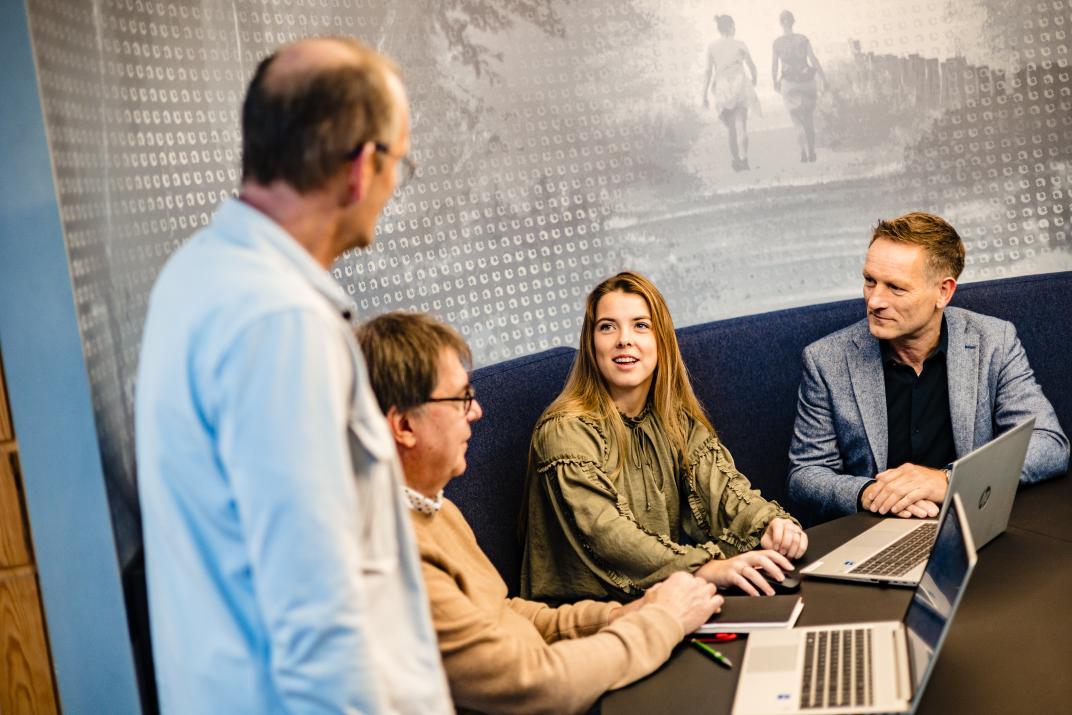 Vier collega's zittend op een bank met laptops op tafel