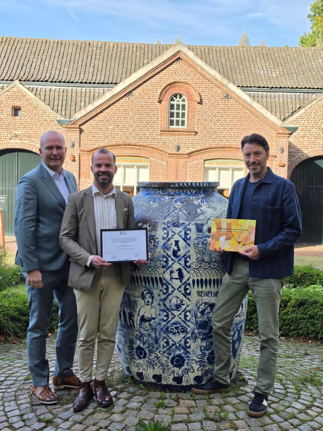 Foto van drie wethouders met boek en certificaat